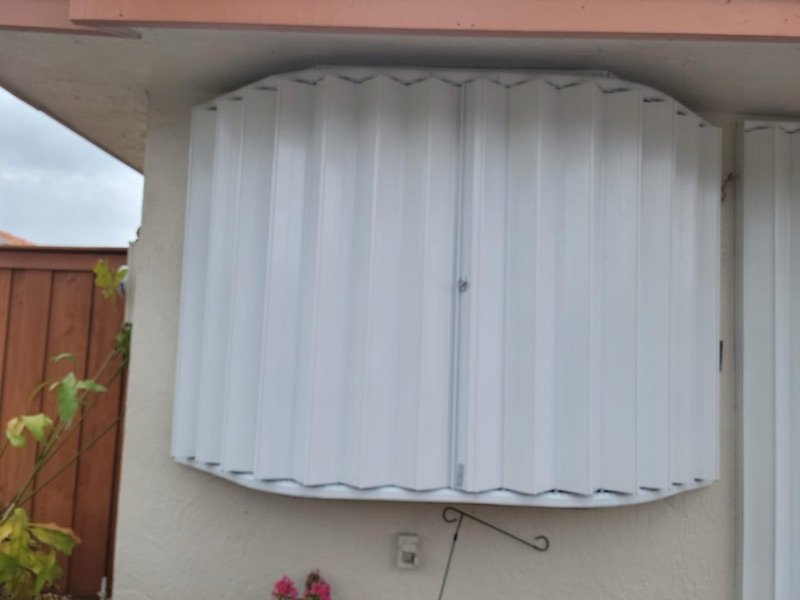 White accordion shutters closed over a bay window in Miami